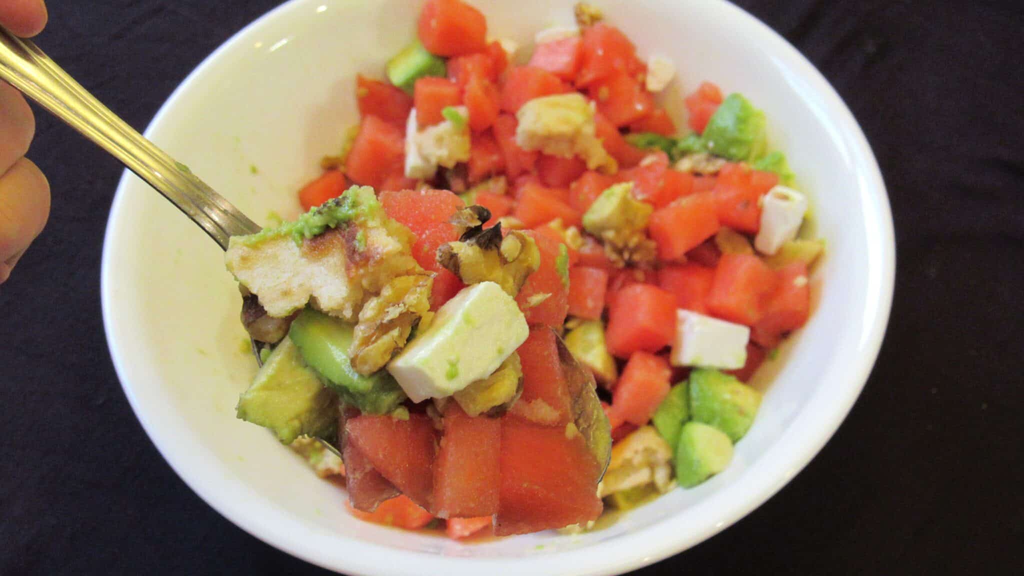 A close-up shot of a spoon full of watermelon avocado feta salad