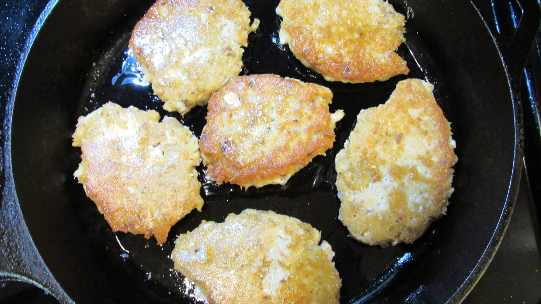 Six salmon patties fried in a cast-iron skillet.