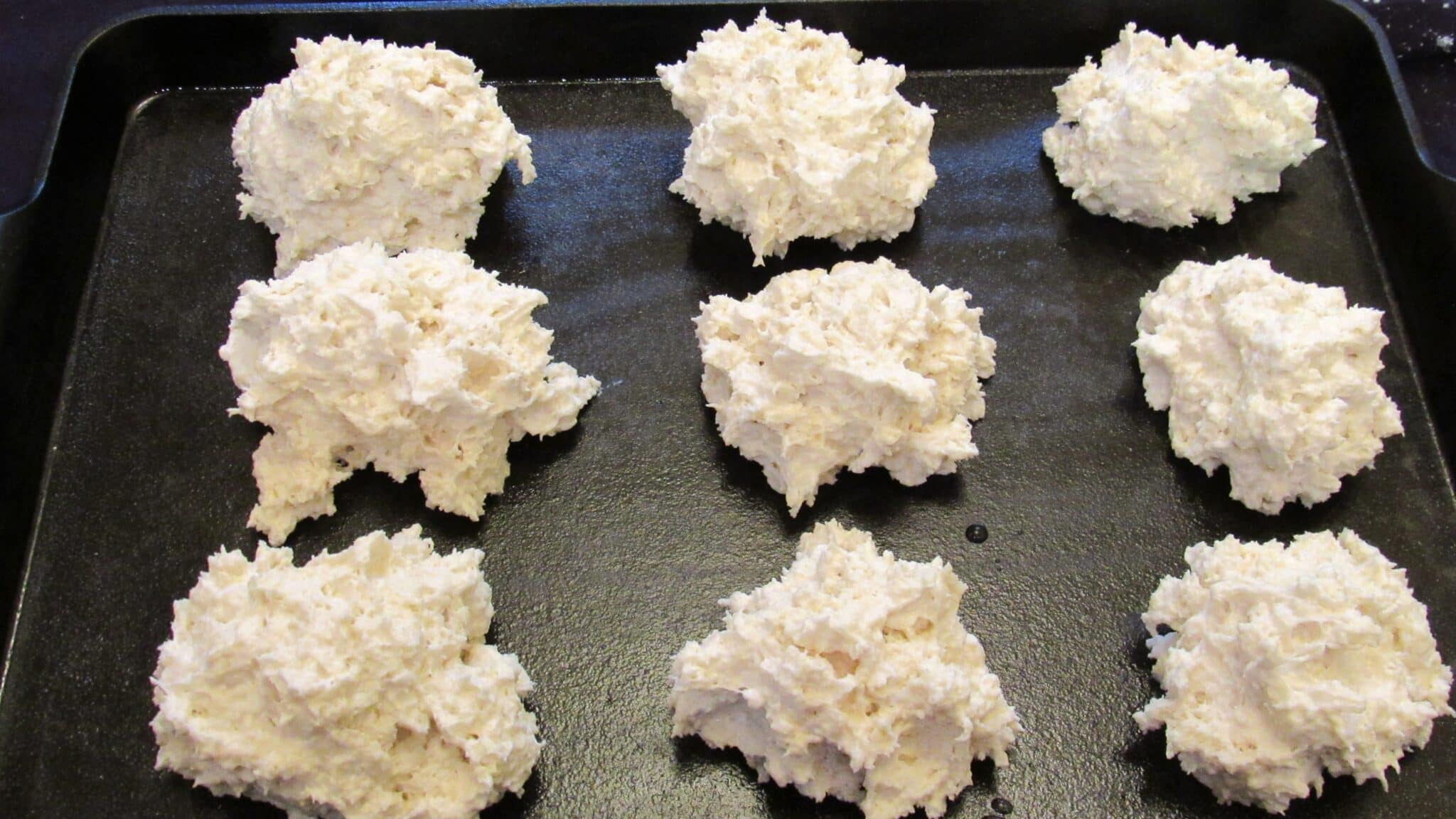 Yogurt biscuits batter is divided into nine pieces on a sheet pan, ready to be baked.