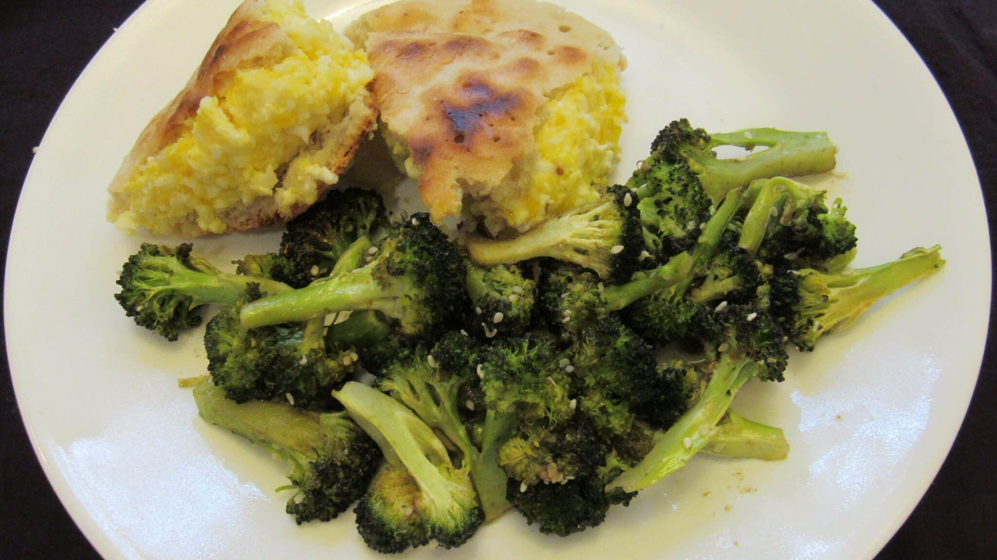 Roasted broccoli is served with an egg sandwich on a white plate for breakfast.