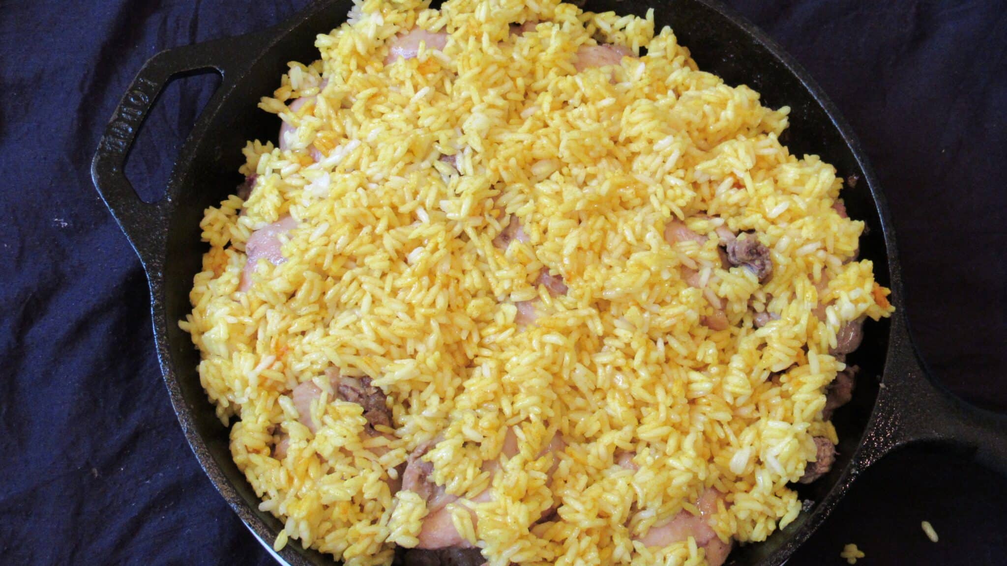 Turmeric rice is layered over the chicken cuts on a cast-iron skillet.