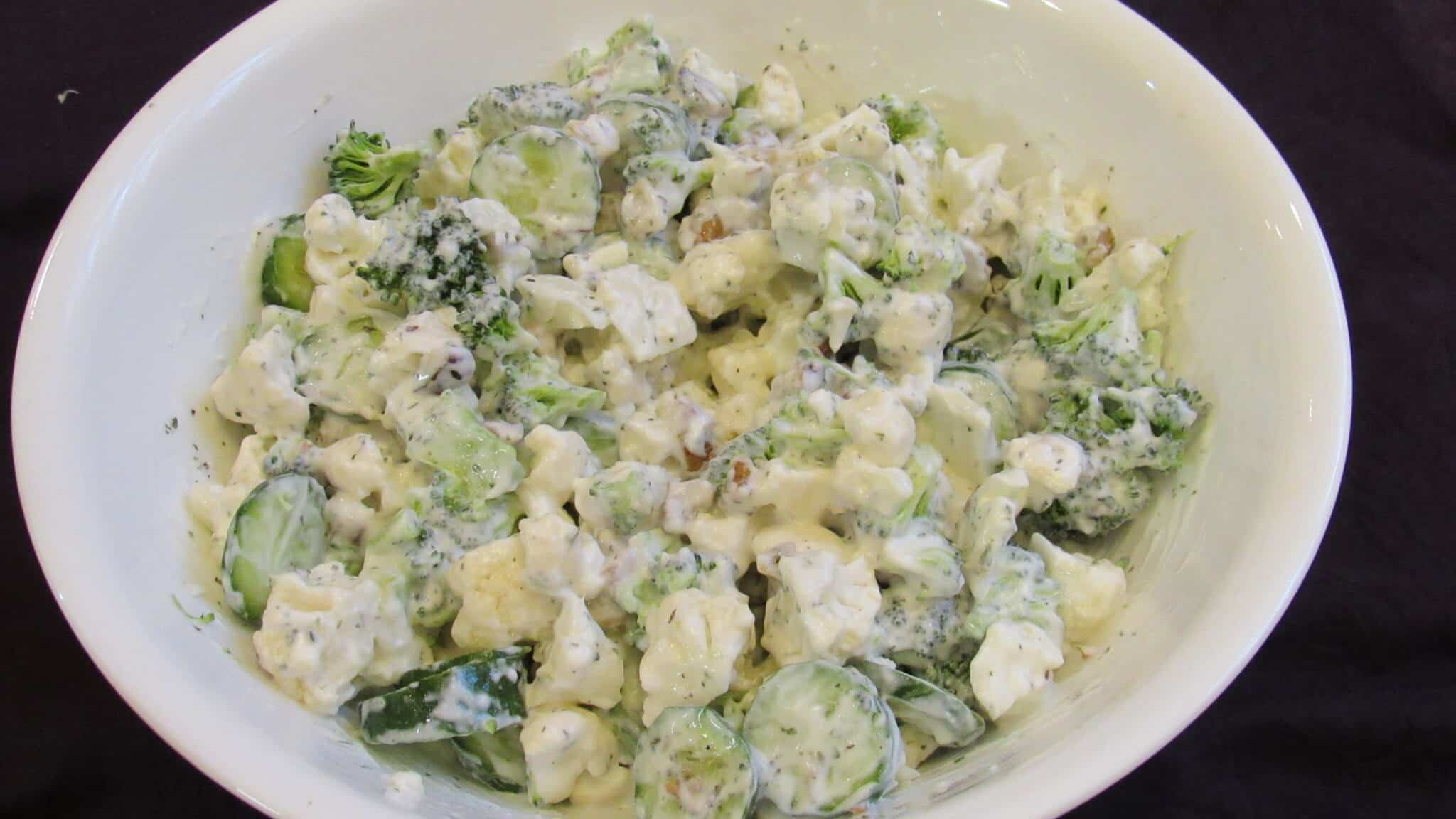 cauliflower broccoli salad is served on a white bowel.