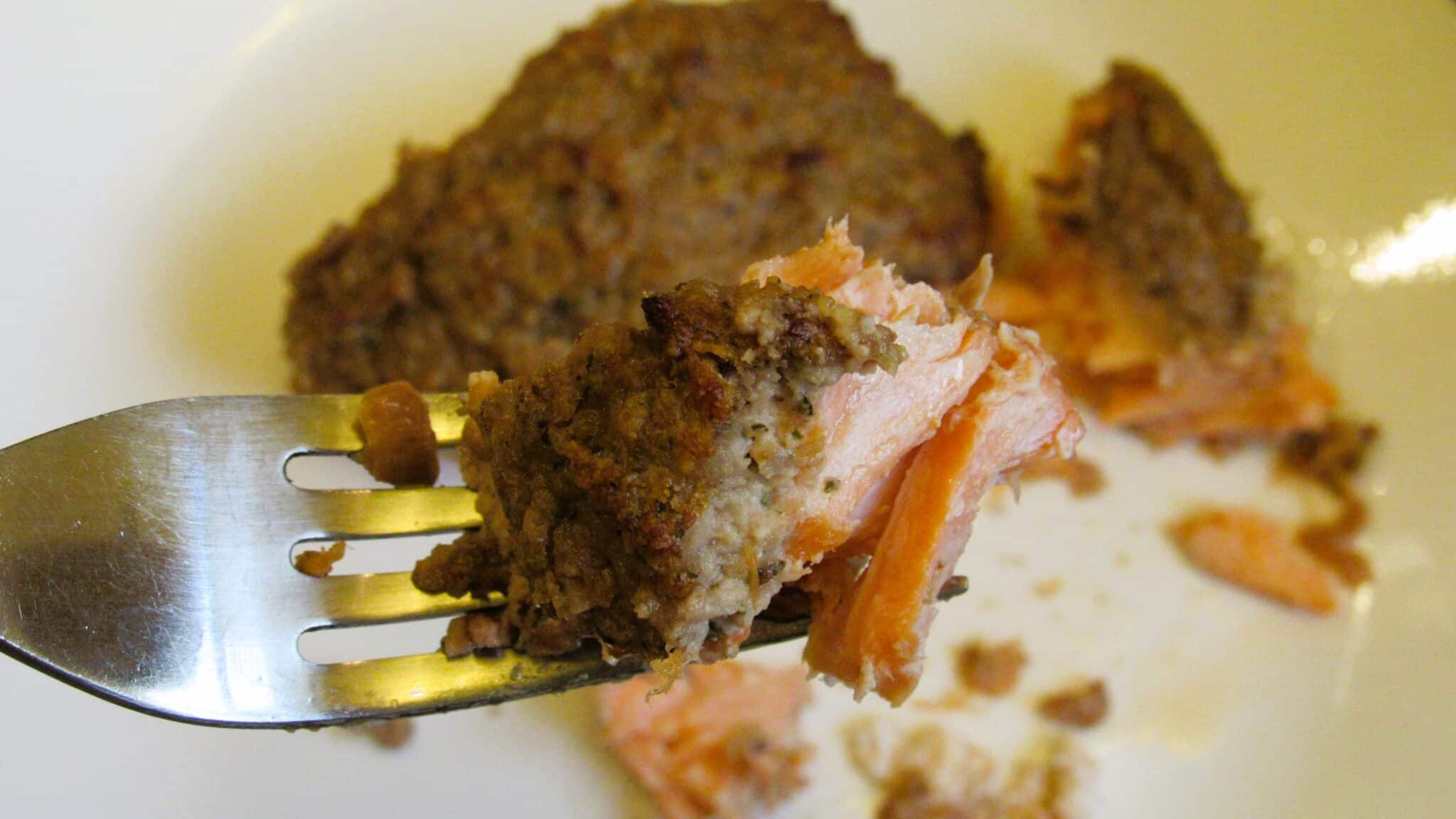 piece of baked salmon with walnut crust on a fork close up image