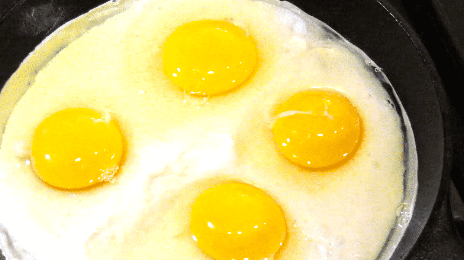 Four eggs cracked on top of sourdough starter in a skillet