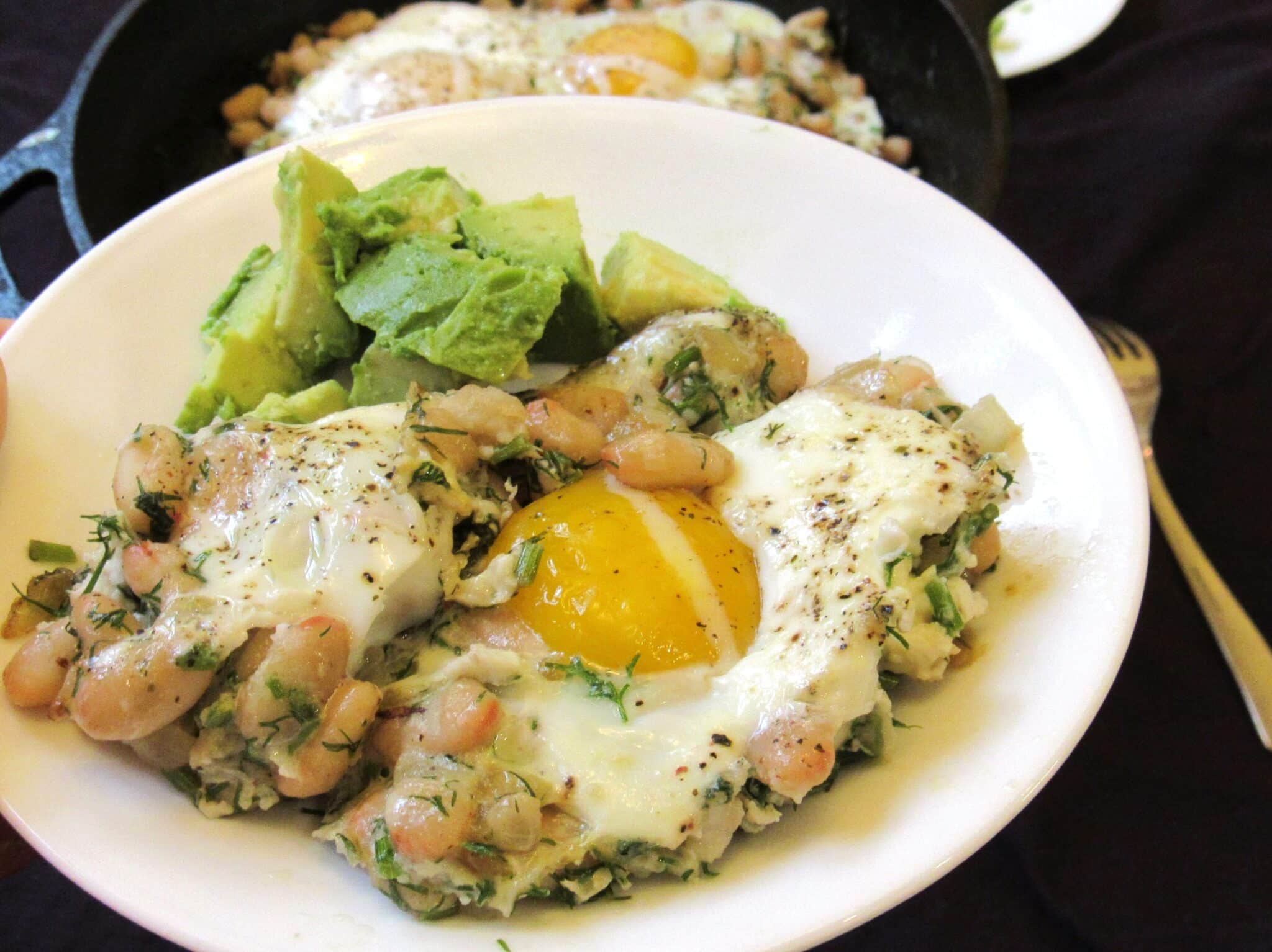 Eggs and beans with avocado slices are served on a white plate.