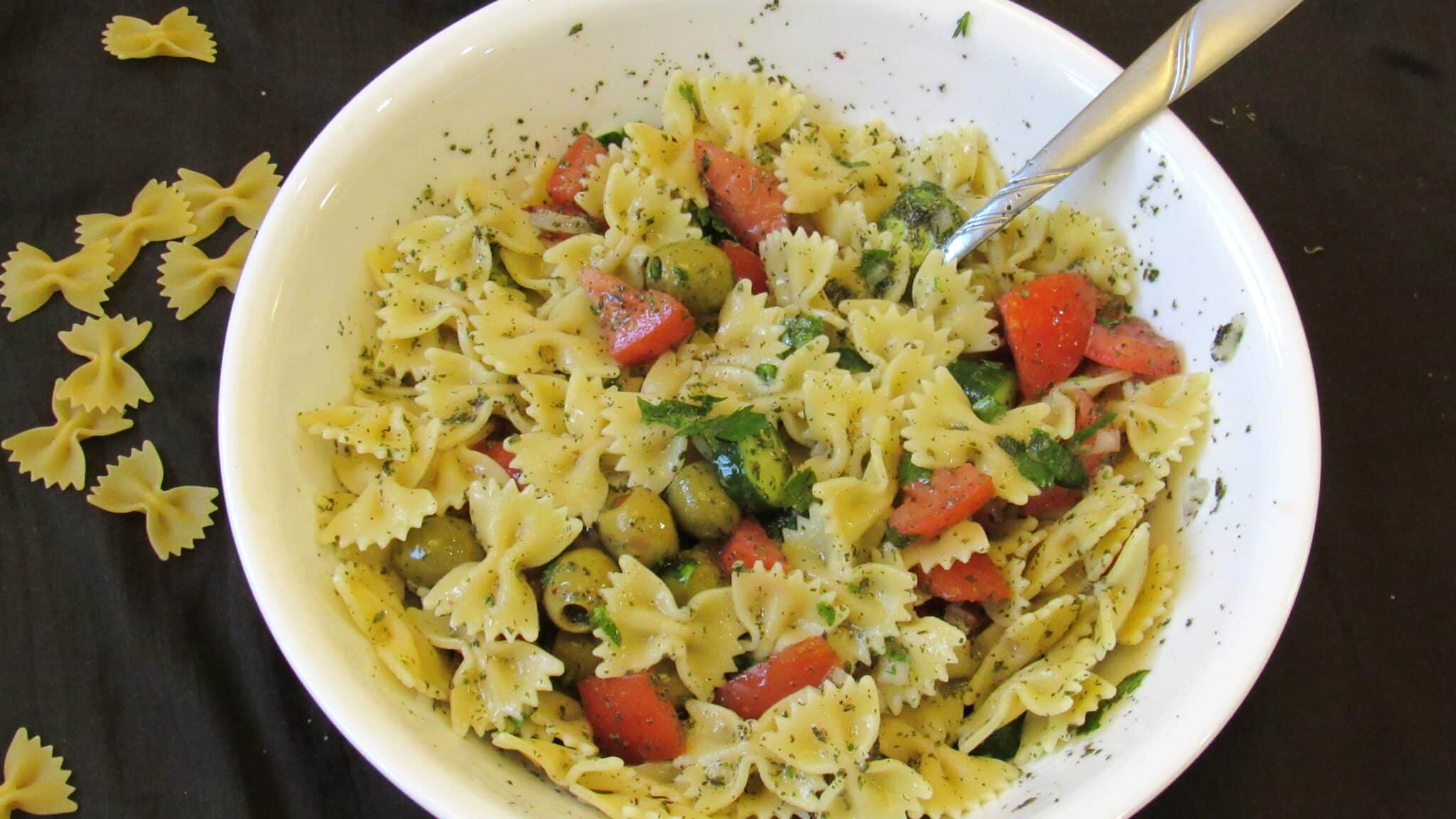 Pasta salad with fresh veggies is served in a white bowl.
