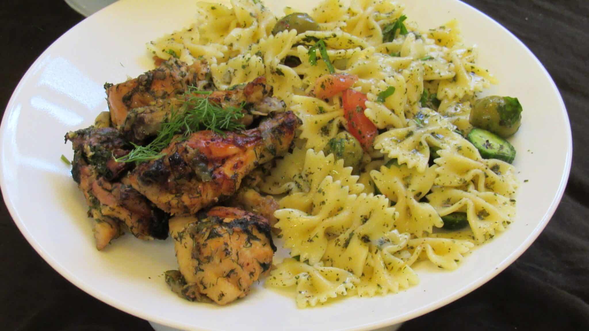 Pasta salad is served with a chicken dish on a white plate.