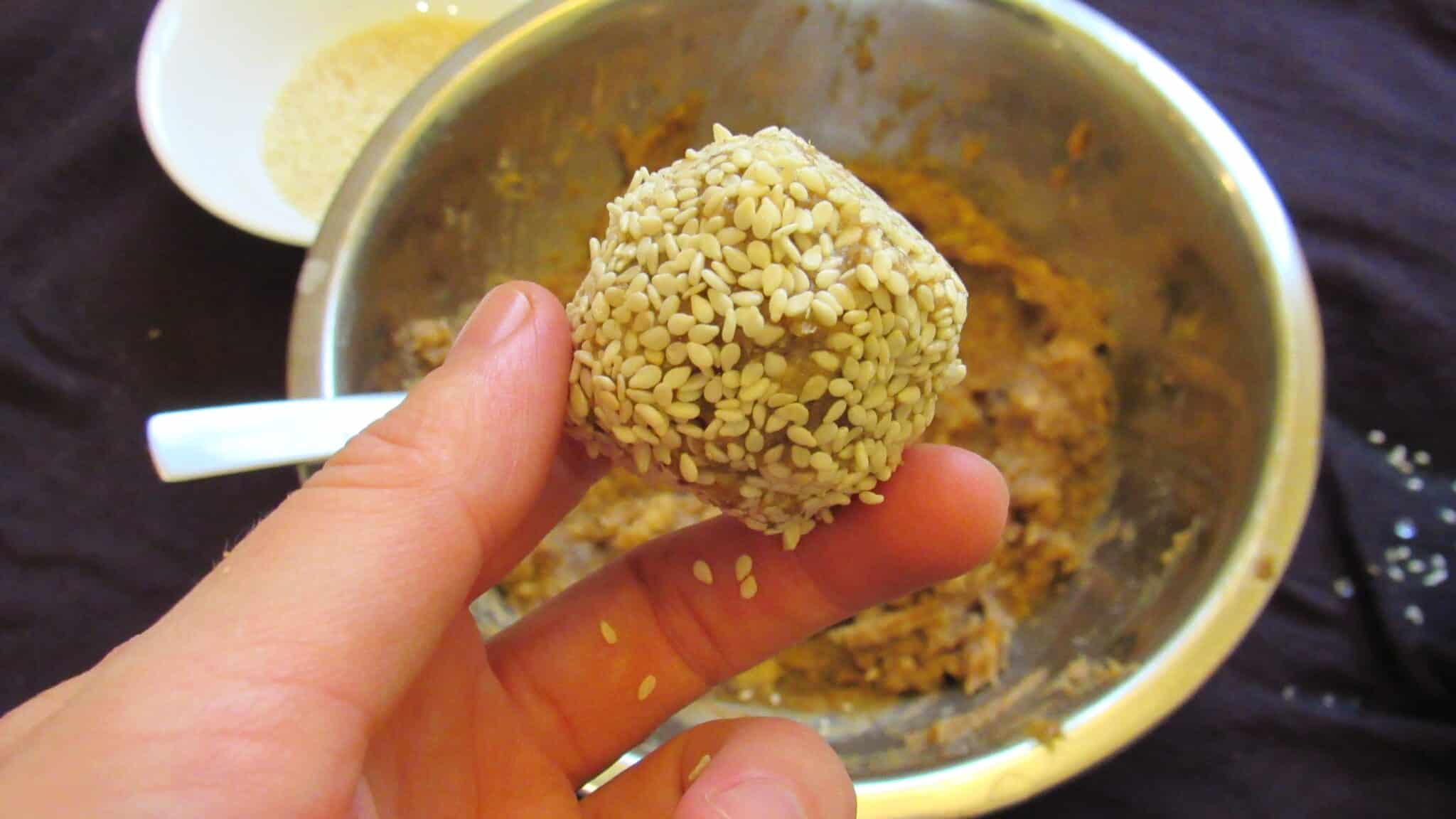 The process of making walnut date balls, a hand holding one is showing how to make it.