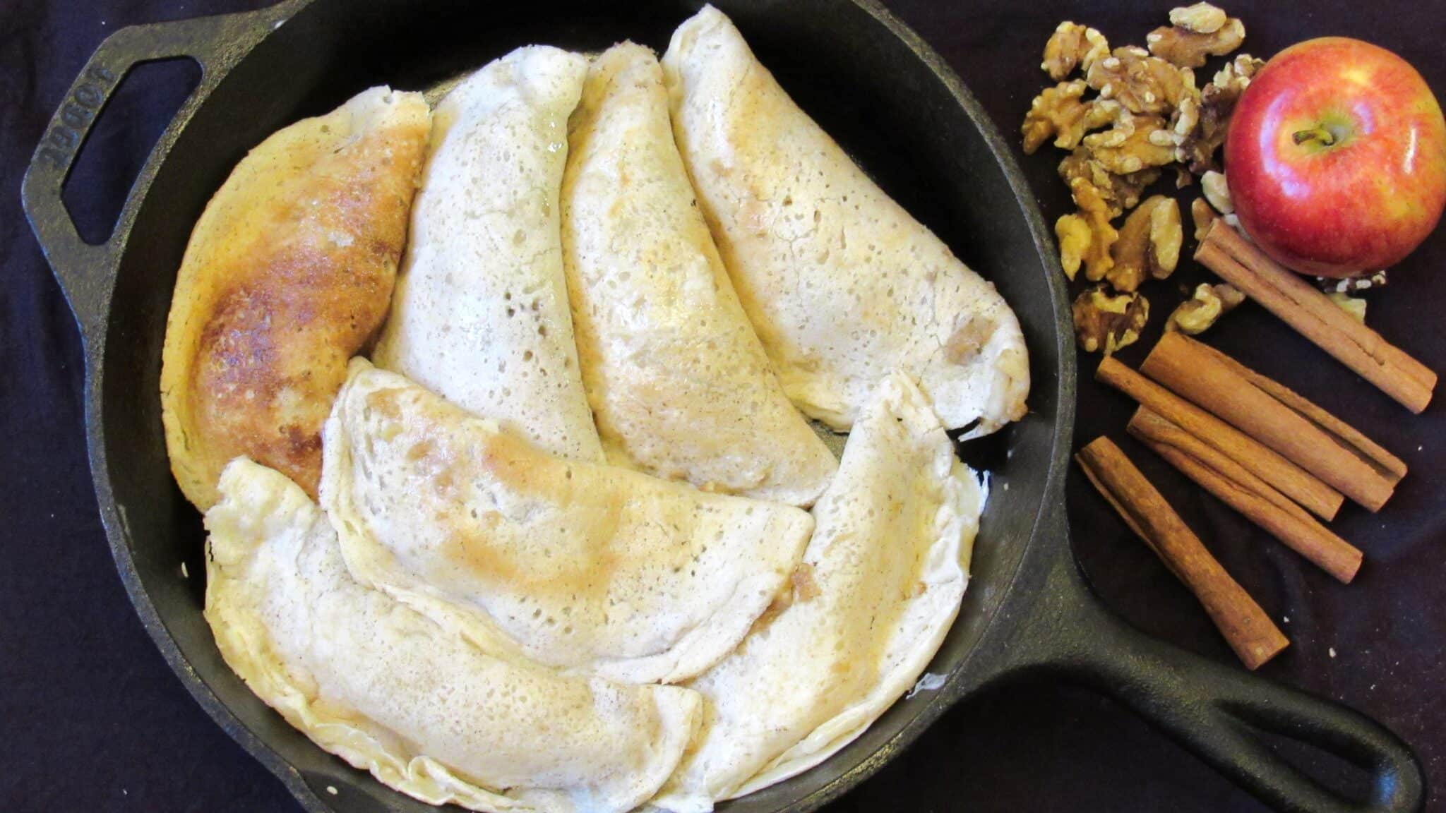 Seven apple enchiladas made with tortillas are placed on a cast-iron skillet and ready to bake in the oven.