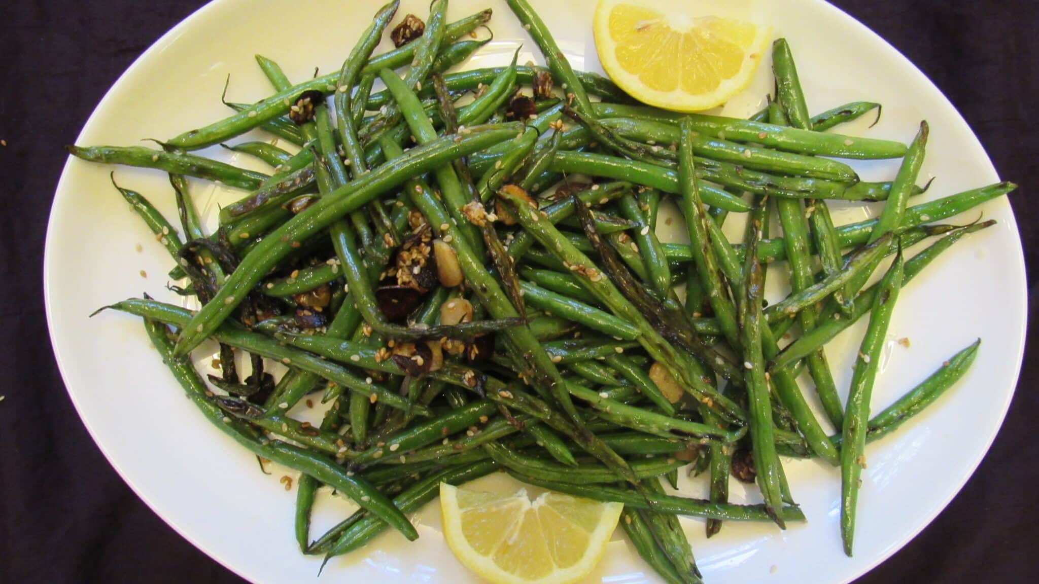 Oven-roasted fresh green beans are served with fresh lemon cuts on a white plate-Top view picture shot.
