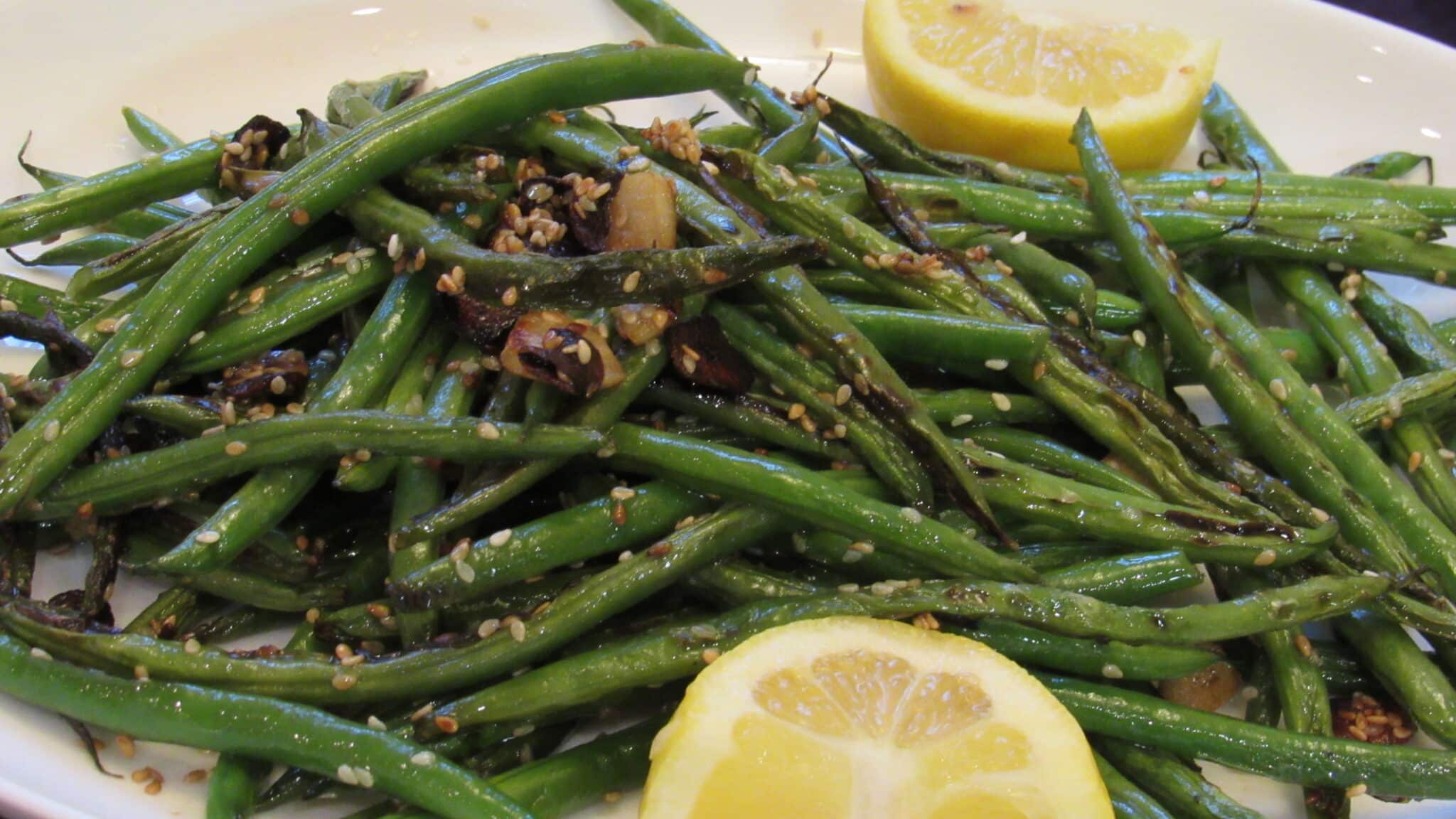 garlic sesame green beans are garnished with fresh lemon juice and served on a white plate.