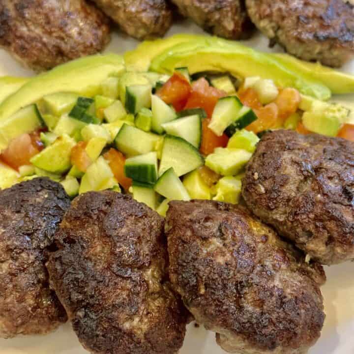 Eight burger patties with fresh avocado salad on a white platter