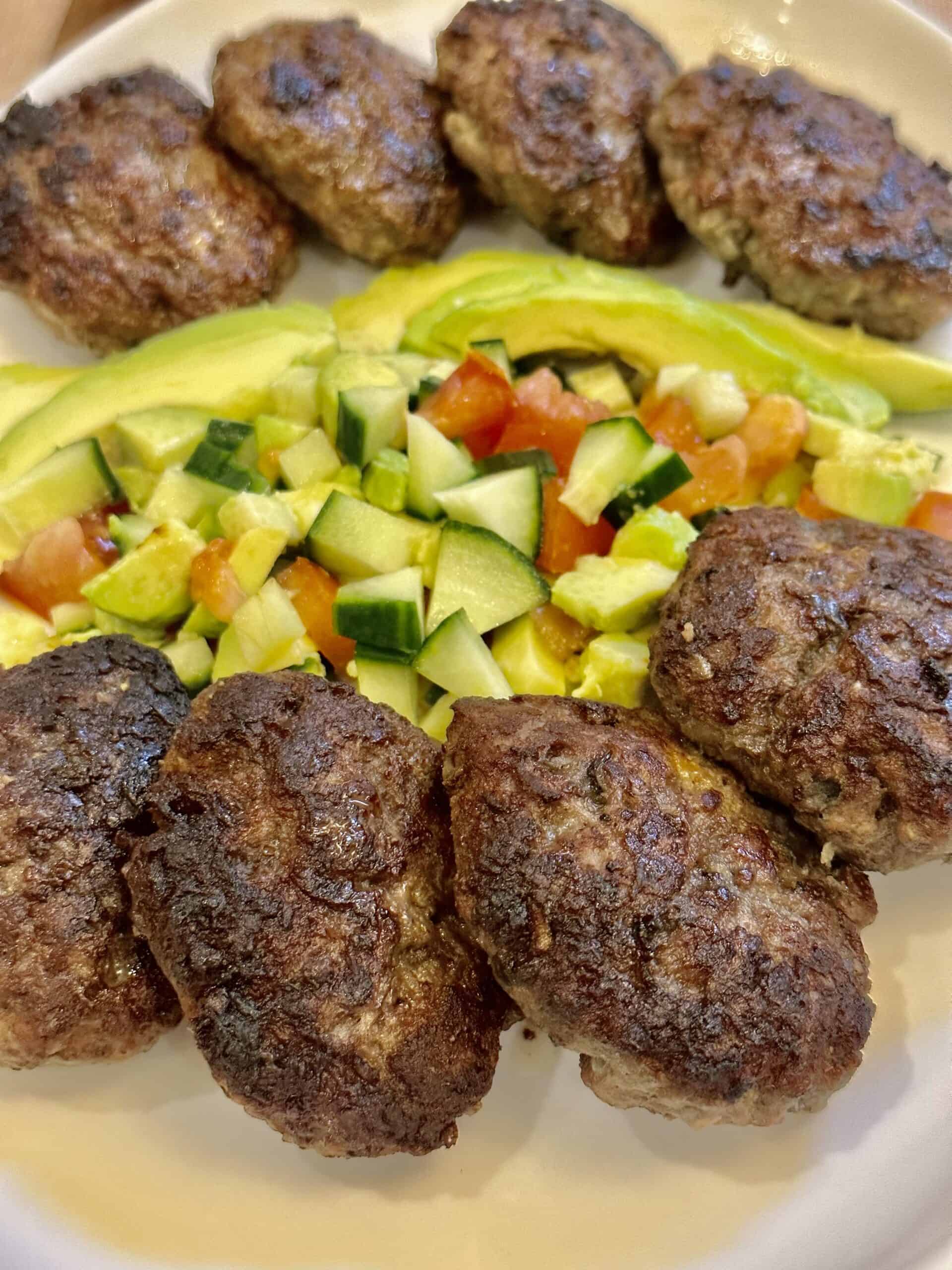 Eight burger patties with fresh avocado salad on a white platter
