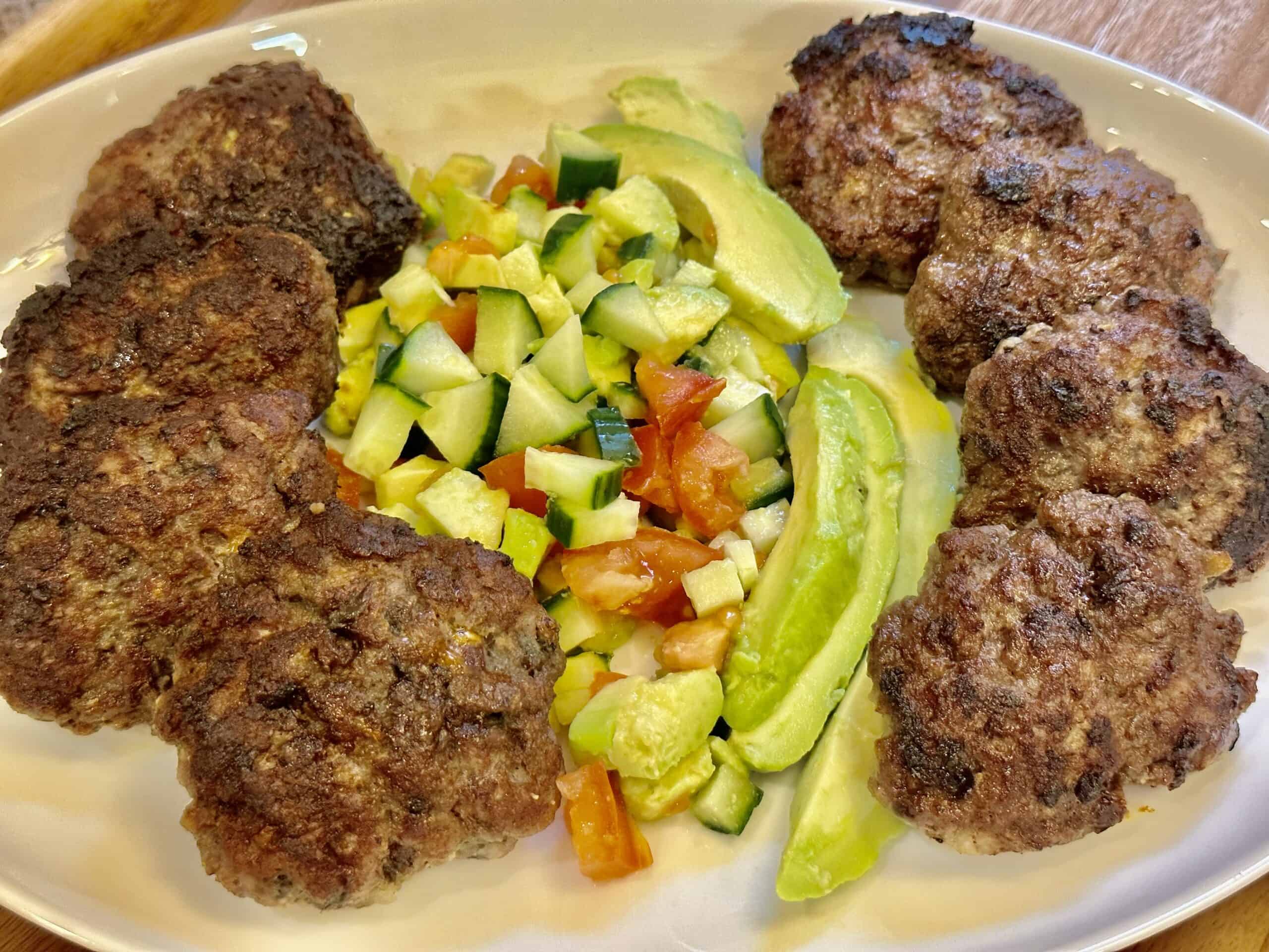 Eight extra lean ground beef burger patties served with avocado salad on a white platter.