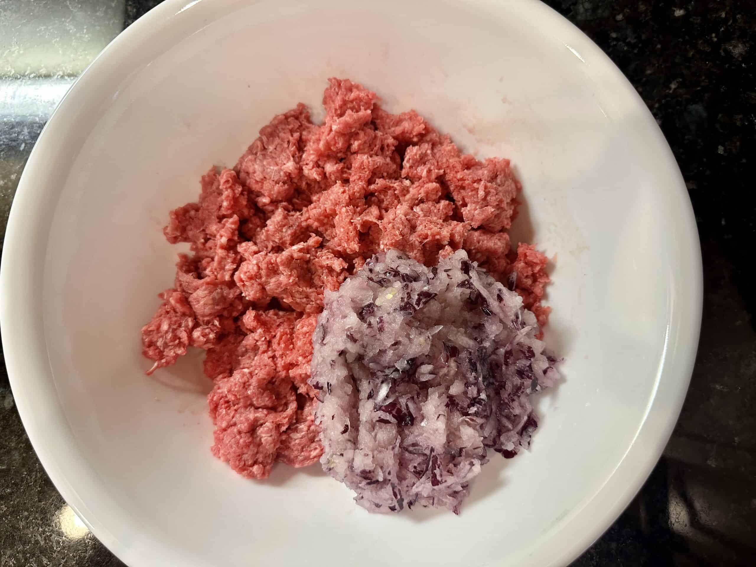 Extra lean ground beef and grinded onion in a white bowl.