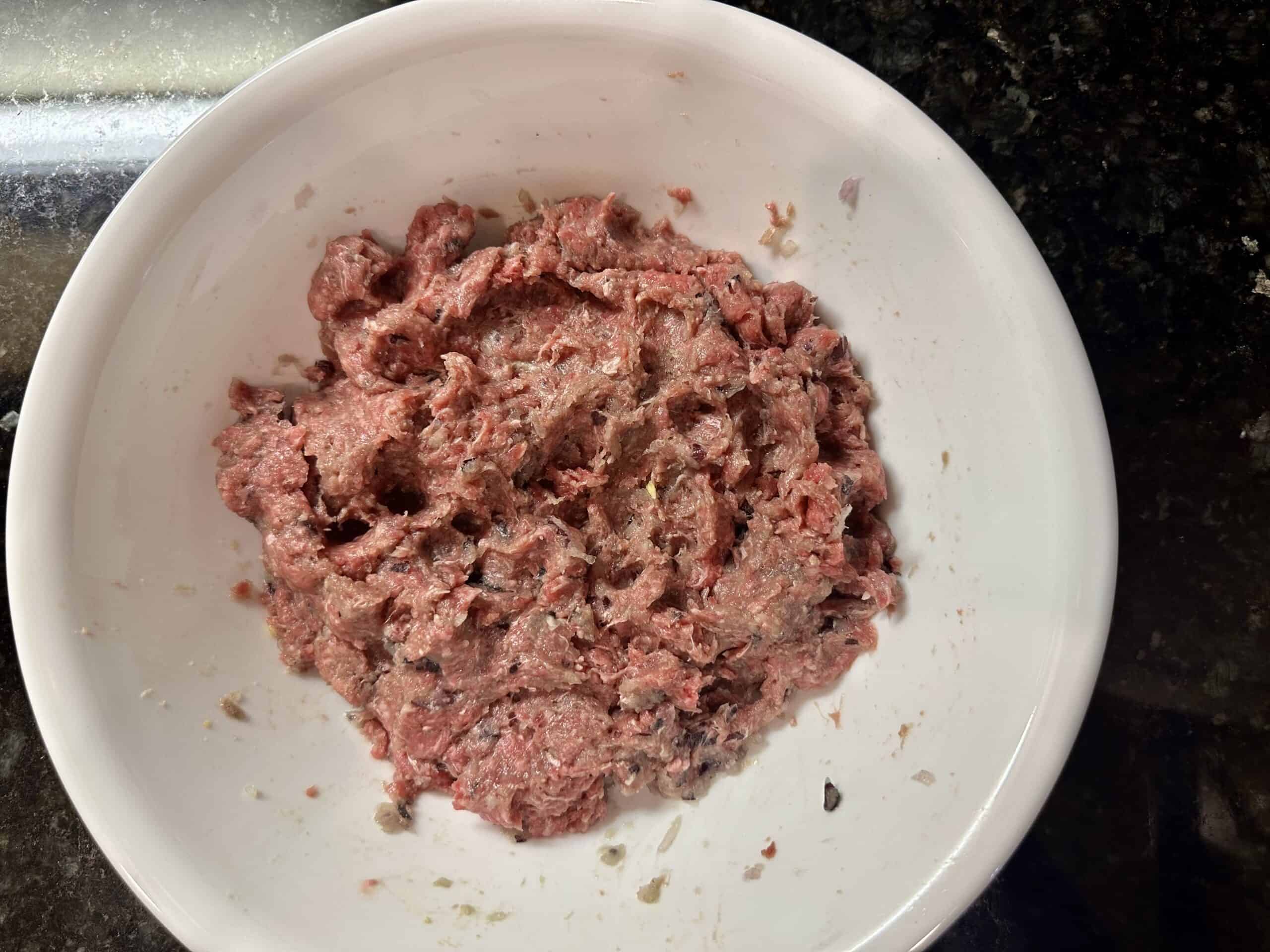 Mixed lean ground beef with onion and seasoning in a white bowl