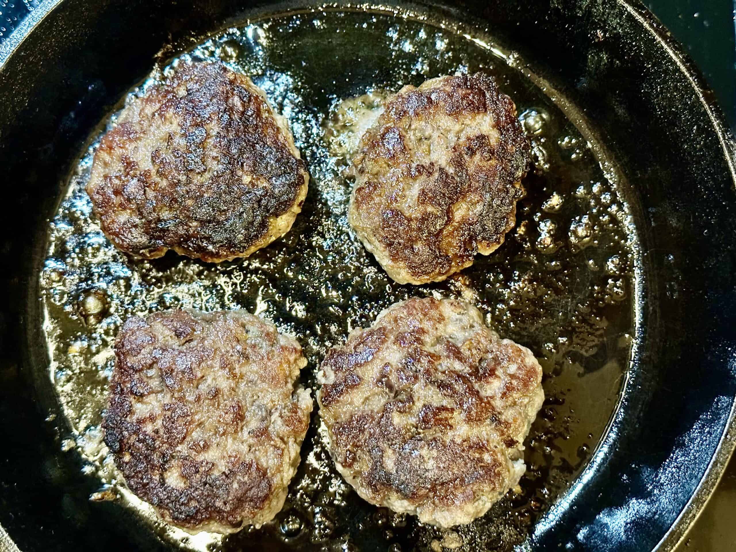 Four extra lean ground beef burger patties on a hot cast-iron skillet.