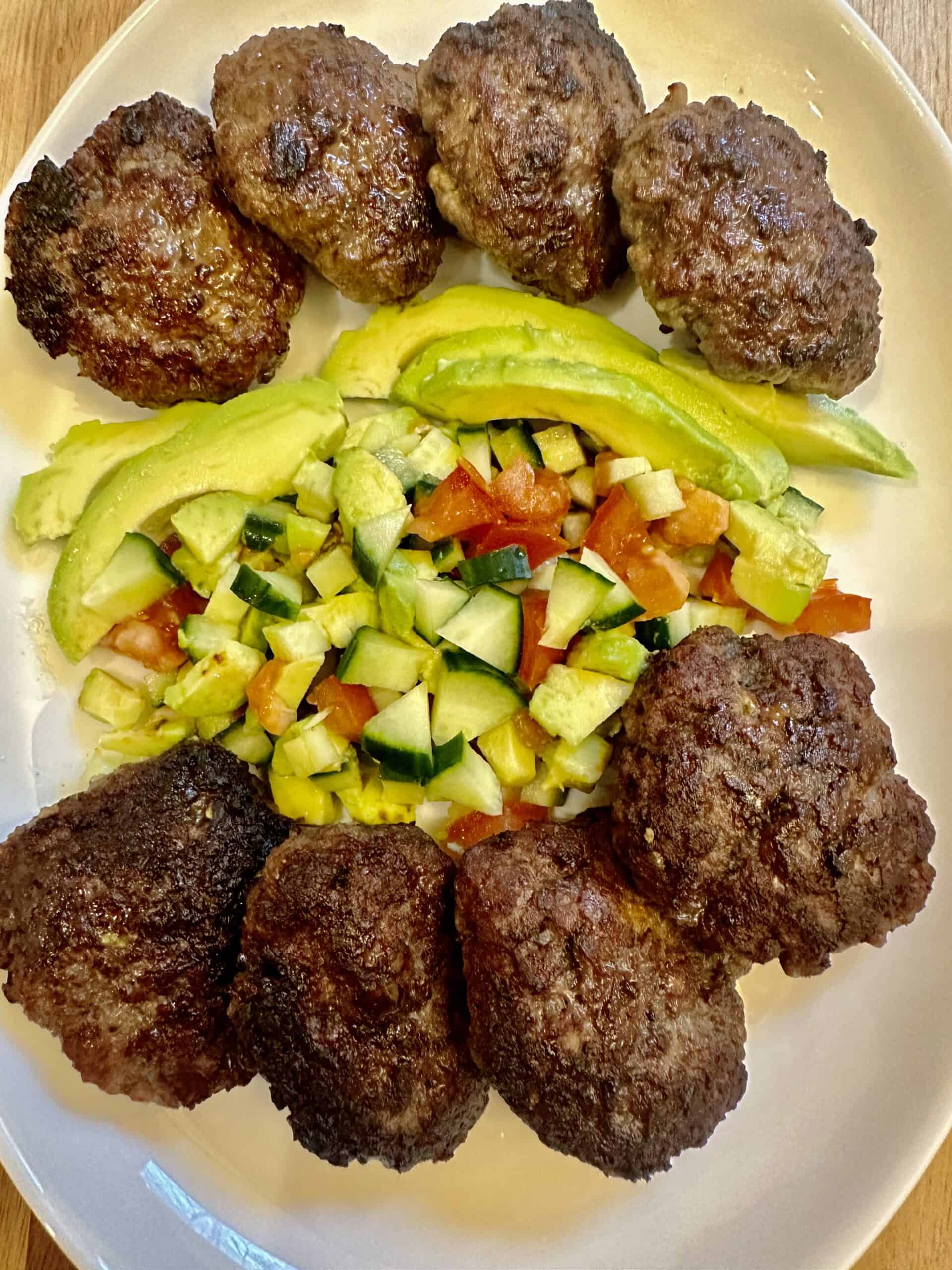 Eight burger patties with fresh avocado salad on a white platter.