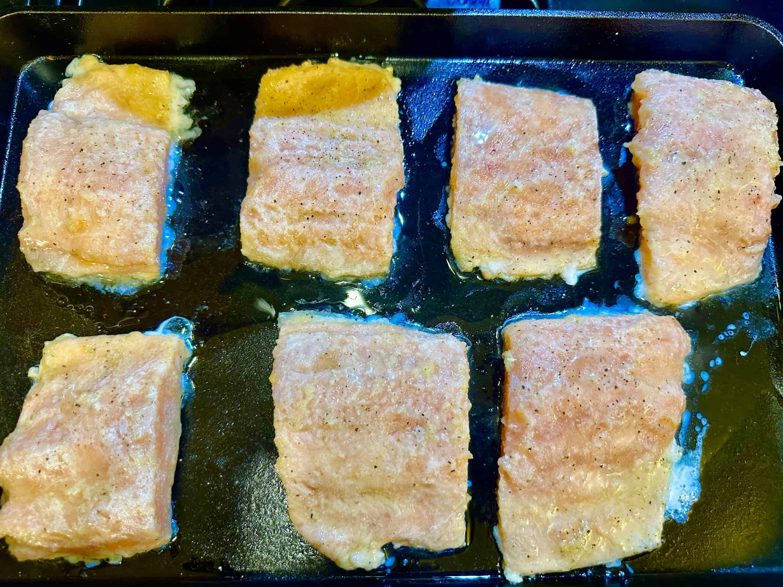7 seasoned frozen salmon fillets on a hot cast iron skillet.