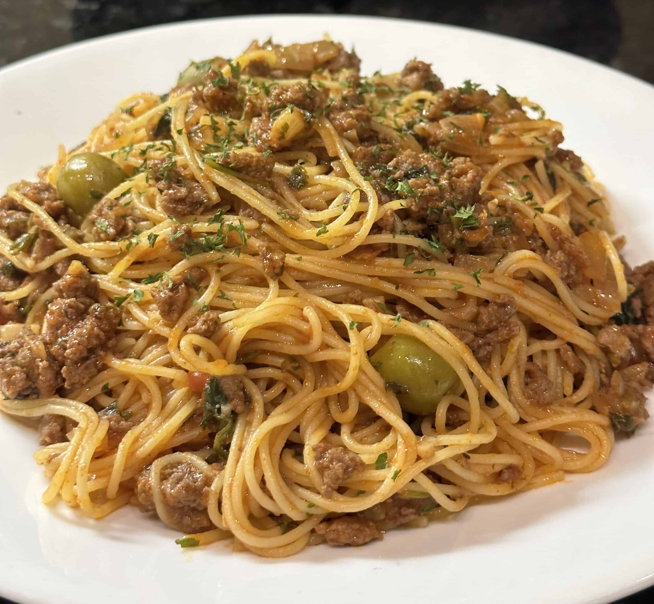 Angel hair pasta with ground beef is served on a white plate.