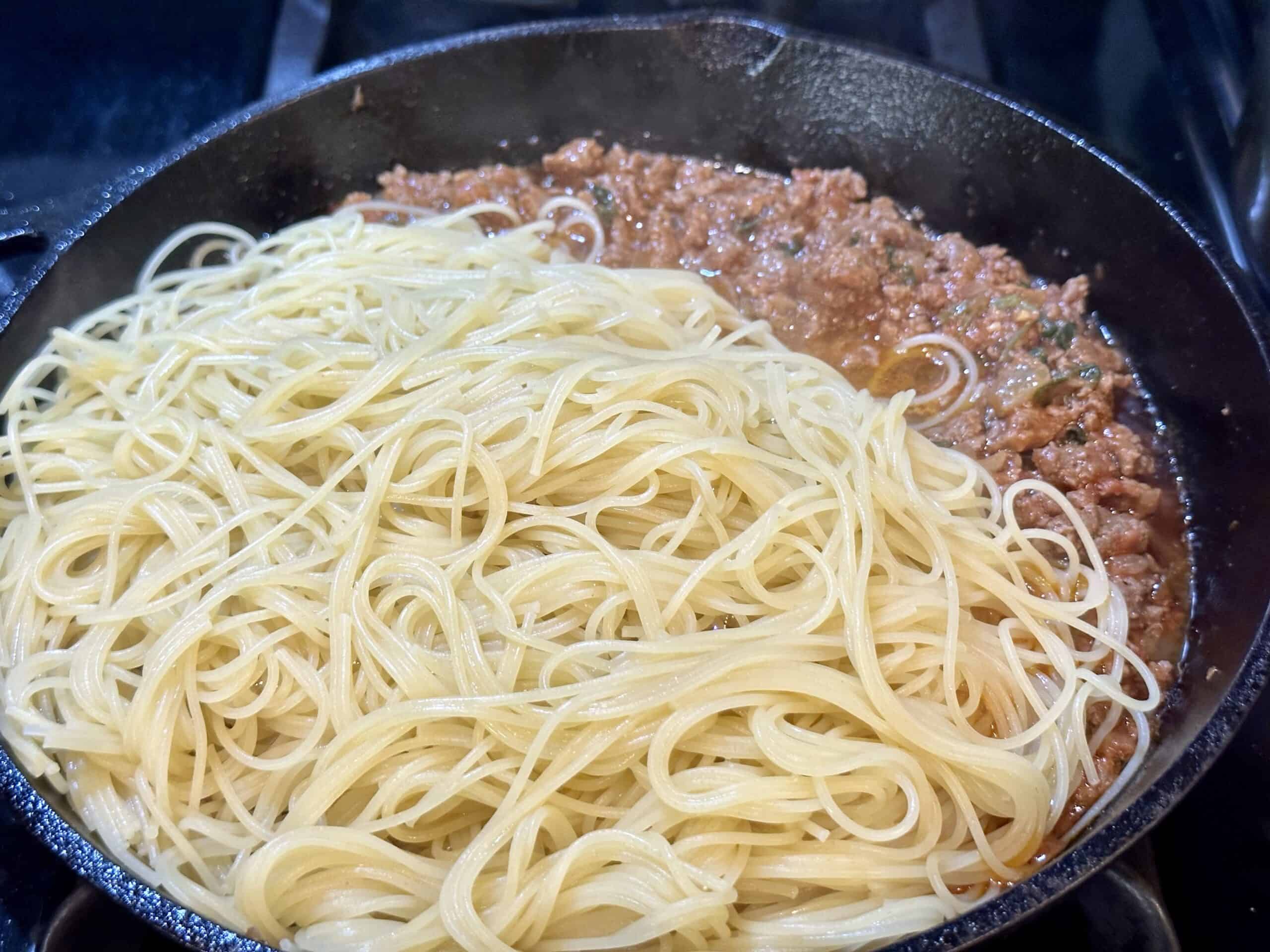 cooked angel hair pasta and pasta sauce with ground beef on a skillet.