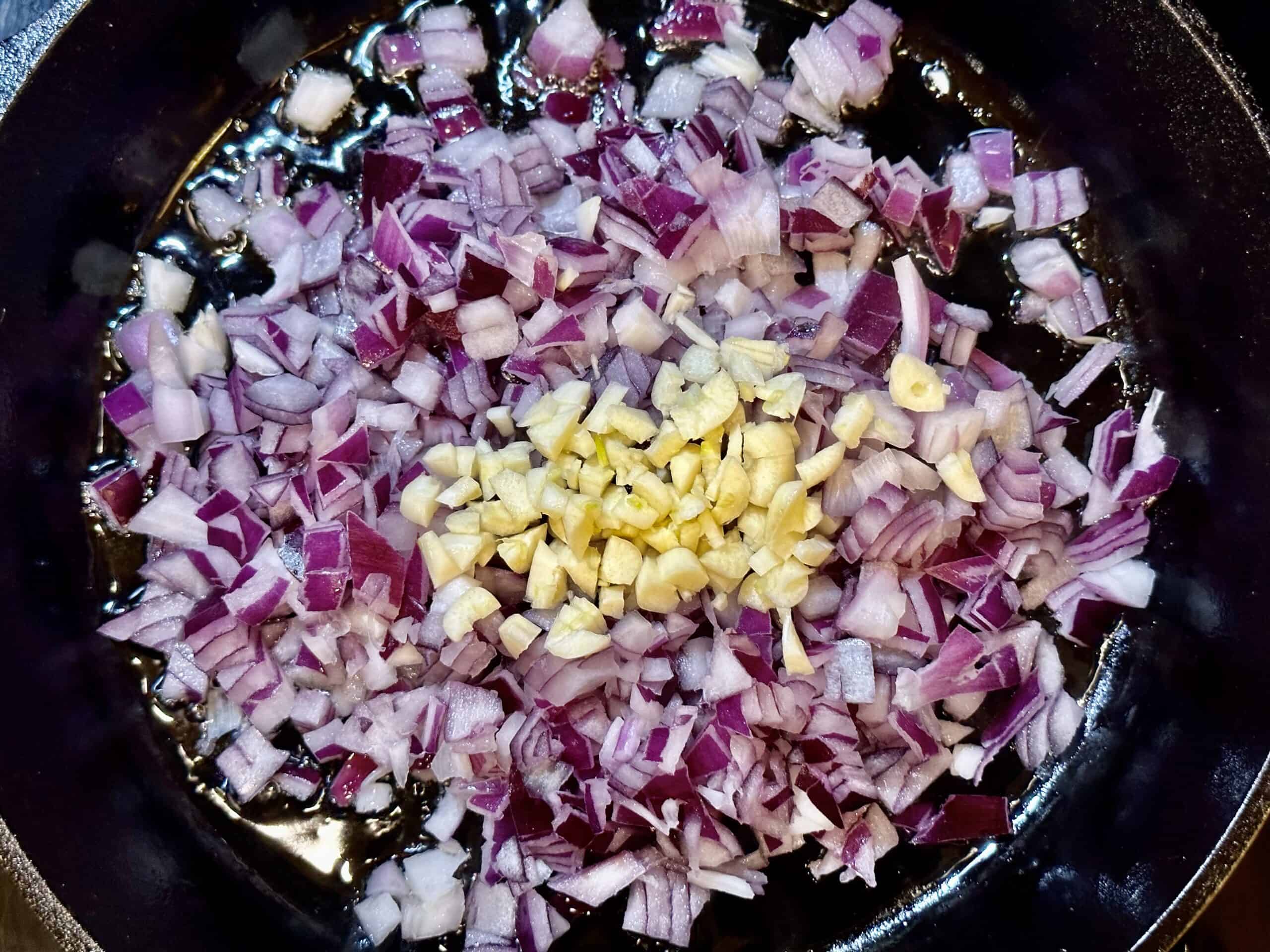 Process shot of chopped onion and minced garlic in a skillet.