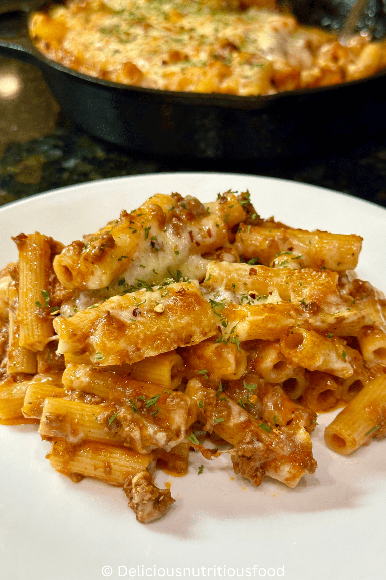 Rigatoni al forno is served on a white plate. garnished with parsley and red pepper flake.