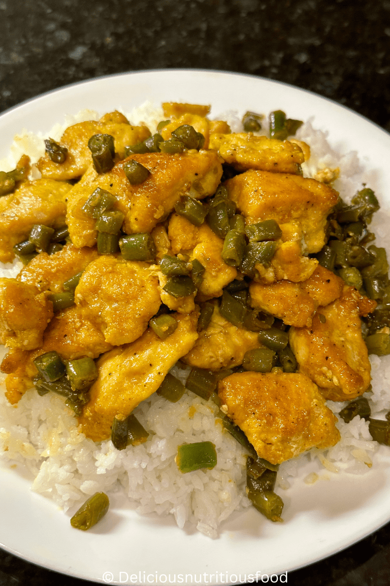 Turmeric black pepper chicken is served with white rice on a white plate.