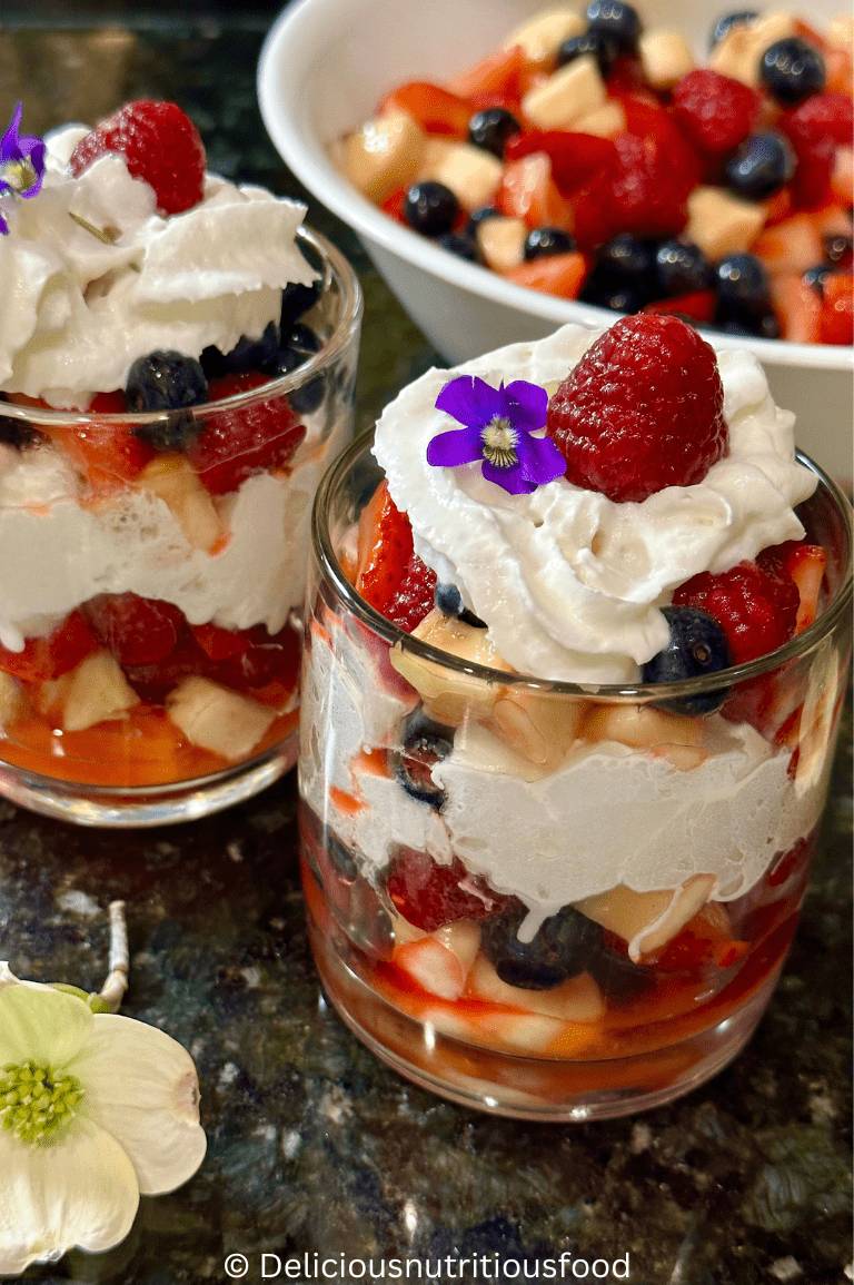 Macedonia di frutta (Italian fruit salad) is served in two glass cups and garnished with whipped cream.