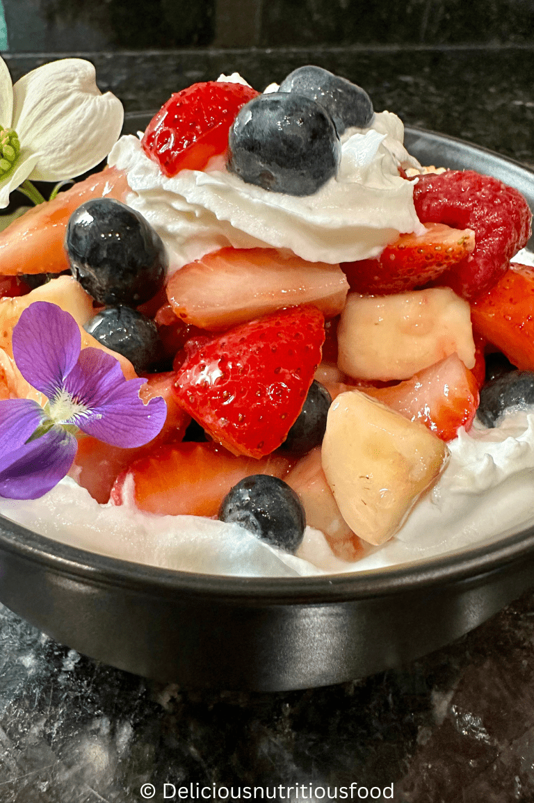 Macedonia di frutta (Italian fruit salad) is served in a bowl and topped with whipped cream.